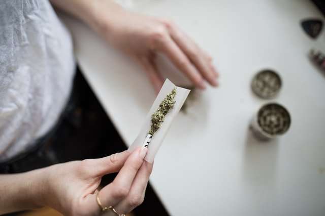 woman-placing-weed-and-dried-shrooms-in-a-paper-roll